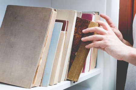 Man chose book from bookshelf. Image performed in vintage stylization.の写真素材