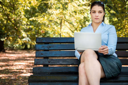 Sexy young businessgirl works with her laptop on the bench in the parkの写真素材