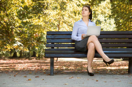 Sexy young businessgirl works with her laptop on the bench in the parkの写真素材