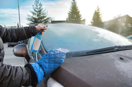 Man uses defroster spray to remove frost from the car windshieldの写真素材