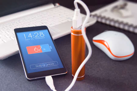 Phone charging with energy bank over the desk. Depth of field on smartphone lock screen graphically created の写真素材