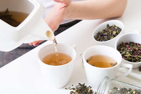 Woman poured hot green tea into cups and different kind of herbs on wooden tableの写真素材