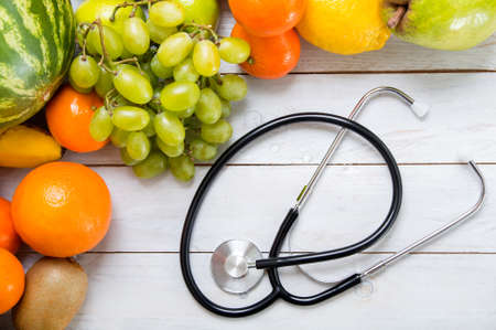 Fruits and stethoscope on white wooden table. Concept of diet and healthy lifestyleの写真素材