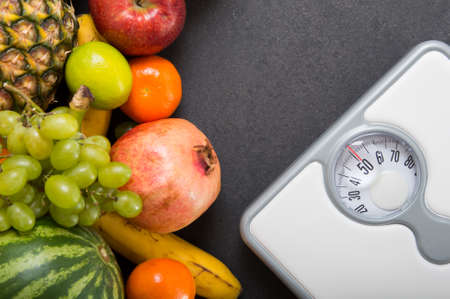 Stack of fruits and white weight scale on stone countertop . Concept of diet and healthy lifestyleの写真素材