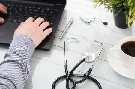 Doctor's hands on laptop and a stethoscope on the desk.の写真素材