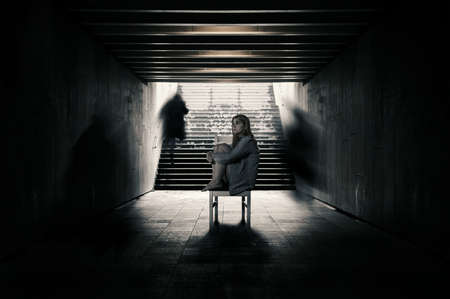 Young woman alone in a tunnel and strangers pass beyond.の写真素材