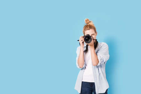 Young blonde photographer is taking a photo. Model isolated on a blue background with copy spaceの写真素材