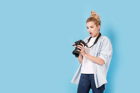 Young blonde photographer is shocked about photo she made. Model isolated on a blue background with copy spaceの写真素材