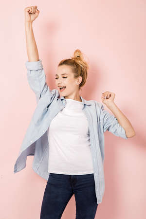 Young woman in a triumphal gesture on a pink backgroundの写真素材
