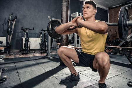 Healthy young man with curl bar performs squats. Photos taken on an atmospheric old gym in a vintage atmosphereの写真素材