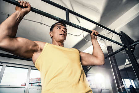 Healthy young man is exercising at the gym, lifting on the gymnastic bar. Photos taken on an...
