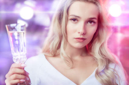Young adorable woman celebrates carnival in the spotlight with a glass of champagneの写真素材