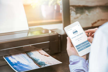Man configures the connection of a mobile phone with a wireless printerの写真素材