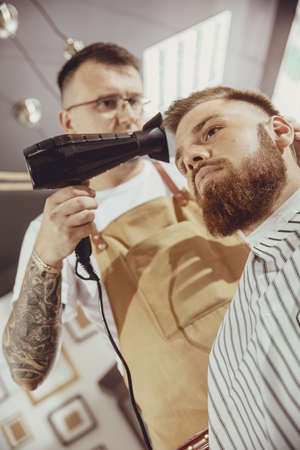 Male hairdresser dries hair of his client. Photo in vintage styleの写真素材
