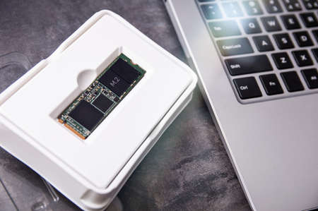 Modern NVMe SSD M.2 drive packed in a factory box lies next to an ultrabook