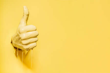 Hand showing the like sign comes out of the yellow wall