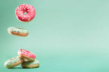 Donuts with pink and green icing with sprinkles on mint backround with copyspace for your textの写真素材