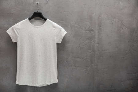 Front side of male white cotton t-shirt on a concrete wall. T-shirt without print and copyspace for...