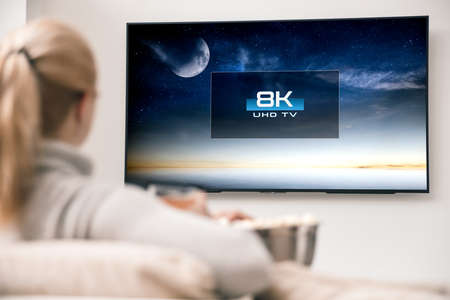 Woman watches tv with 8k ultra hd resolution. Picture on the screen created in graphic software.の写真素材