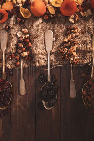Dried fruits and nuts arranged on a spoon, fabric and an old table. Vertical composition in the old style.の写真素材