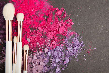 White make up brushes and violet and pink eyeshadows arranged on flat stone