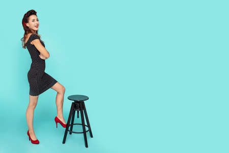 Young pin-up woman holds her leg on the chair. Picture including copy space for textの写真素材