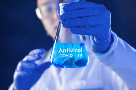 Lab worker holds flask with antiviral medicines. Conception of  studies about coronaの写真素材