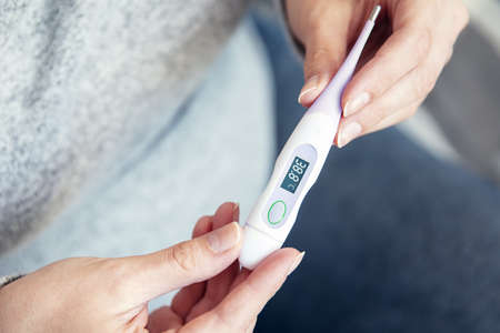 Woman's hands hold thermometer that shows high body temperature