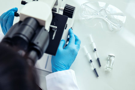 Female scientist uses microscope. Female scientist in protective gloves uses medical microscope with...