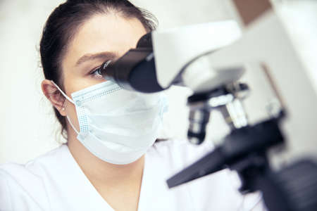 Woman uses a microscope. Female scientist examines sample with medical microscope