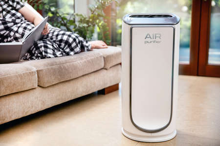 Air purifier cleans up air. Modern air purifier cleans up the air in the living room with woman lying on the couch. logo on the device was created in graphic programの写真素材