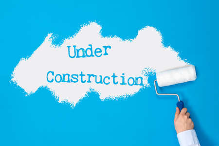 Hand with paint roller paints blue wall and under construction sign on it.