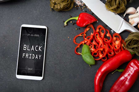 Modern smartphone with black friday banner on the screen lies on countertop with spicy vegetablesの写真素材