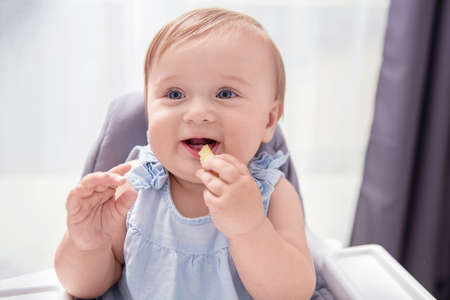 Infant baby girl in blue dress eats crisp and smilesの写真素材