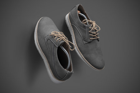Top view of a pair of modern gray suede casual shoes with beige laces and white soles, arranged diagonally on a smooth gray background. Shoe trees are visible inside the shoes, highlighting shape and detail.の写真素材