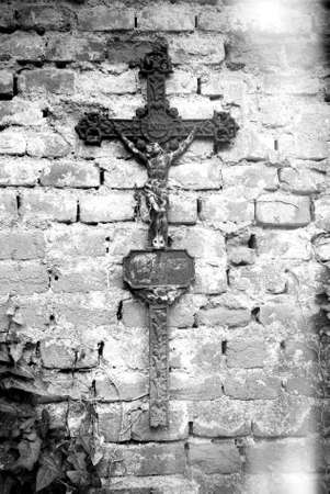 Rusty christian cross with Jesus Christ statue hanging on an old brick wallの写真素材