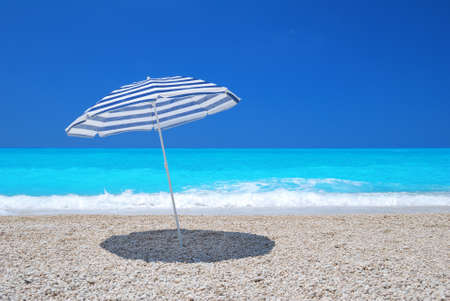 Sun umbrella on a pebble beach with turquoise sea and skyの写真素材