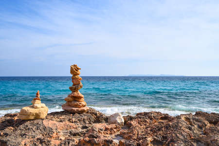 Stone pyramid on the rocky coast of a blue wavy seaの写真素材