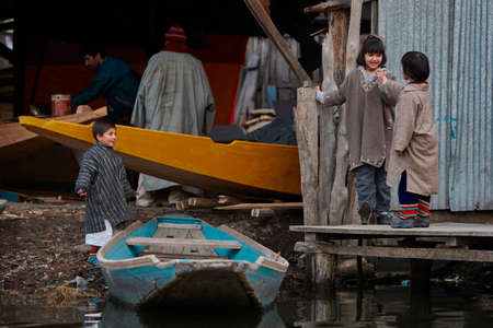 Dal Lake, Srinagar, Kashmir, India - February 15 2012 : Children in national Kashmiri clothes play at the workshop where their parents make boats.のeditorial素材