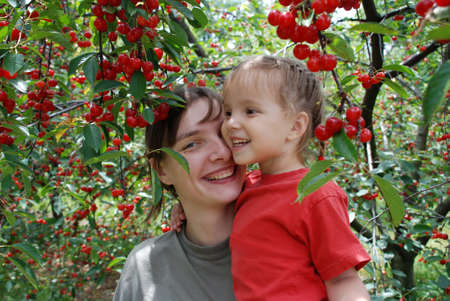 Mother and daughter among the ripe berries of cherry in the gardenの写真素材
