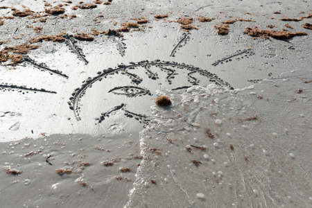 The waves wash away the sun drawn on the sand. Farewell, Summer!の写真素材