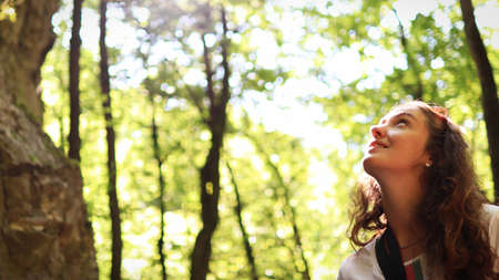 A young woman enjoys the sun's rays shining through the leaves of trees on a trip.の写真素材
