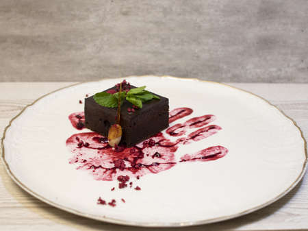 Brownie served on a plate. Brownie is decorated with almond in caramel, mint, raspberries and handprint in cherry cream.の写真素材