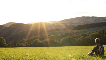A young man sitting in a meadow at sunsetの写真素材