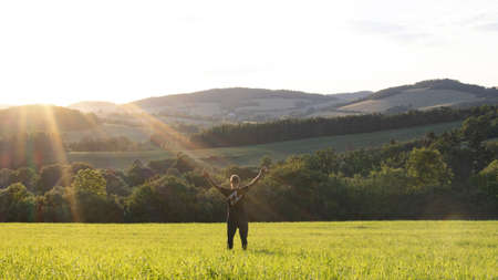 A young man stands in a meadow at sunset