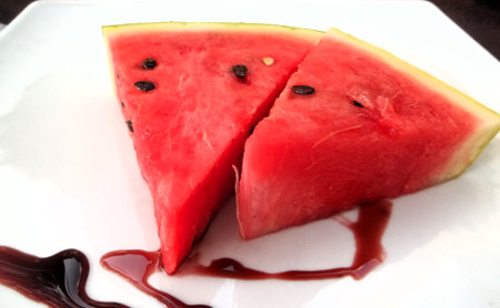 Watermelon slices with berry sauce on a white plate closeup