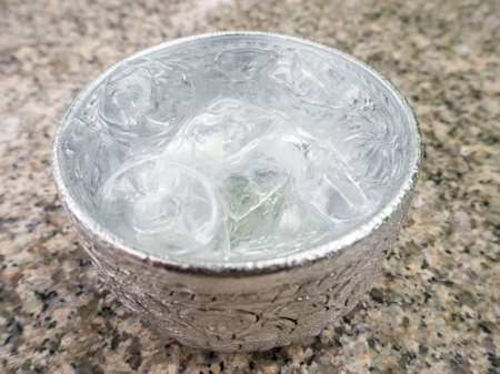Aluminum bowl with water and  ice cube on the dining table in the restaurant, Thai styleの写真素材