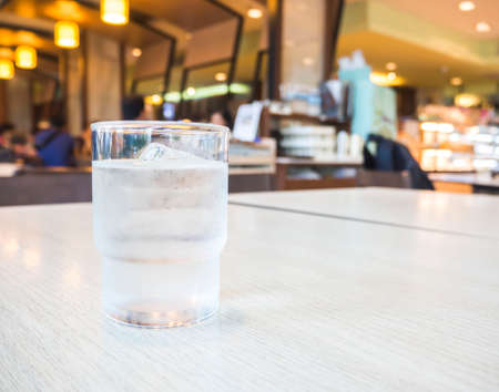 Glass of water with ice cube on wooden table under the lights in restaurantの写真素材