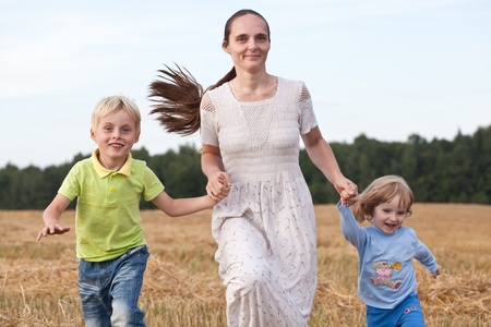 Mother and two children running outdoors smilingの写真素材