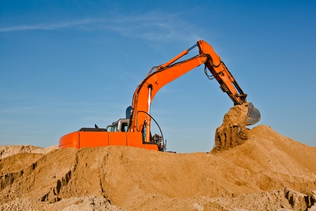 Excavator working in sand pit moving earth by its bucketの写真素材